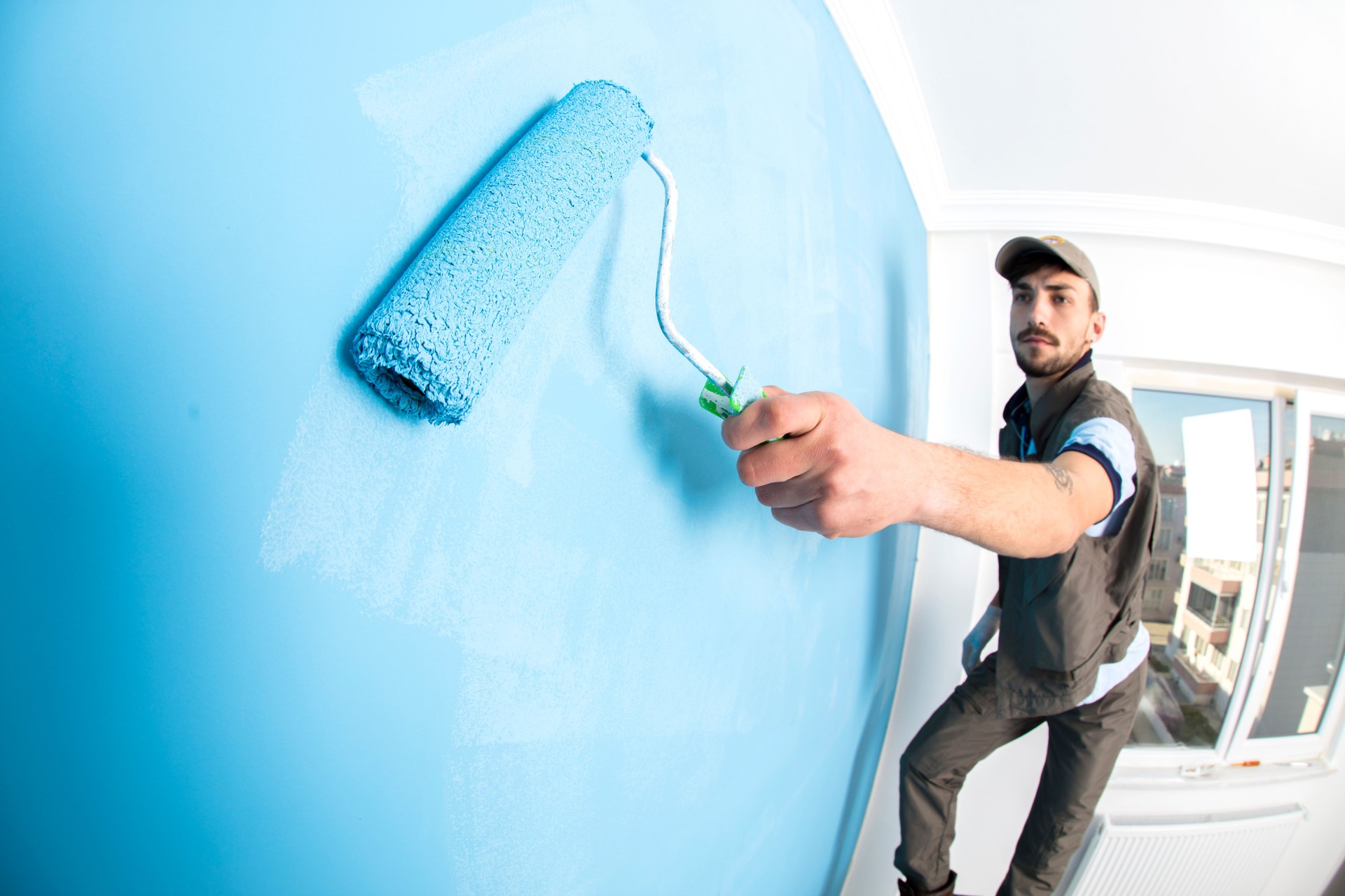 Young man painting a wall blue with a roller